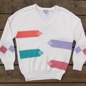 May include: White v-neck sweater with a geometric pattern in shades of pink, purple, teal and orange. The sweater has a diamond pattern on the sleeves.