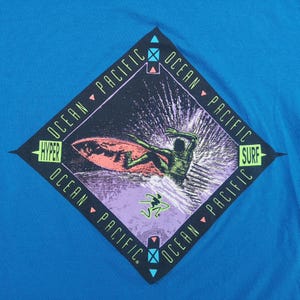 May include: A blue t-shirt with a diamond-shaped graphic featuring a surfer riding a wave. The graphic has the text "Ocean Pacific" repeated around the diamond and "Hyper" and "Surf" at the top and bottom of the diamond.
