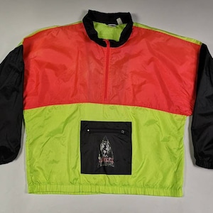 Könnte beinhalten: Windjacke in Blockfarben in Neongrün, Rot und Schwarz. Die Jacke hat einen schwarzen Kragen und Ärmel, eine rote obere Brust und einen neongrünen unteren Bereich. Eine schwarze Tasche mit Grafik befindet sich auf der unteren Vorderseite. Die Jacke hat einen Reißverschluss.