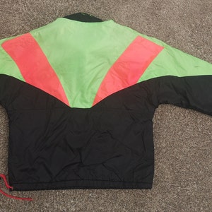 Pode incluir: Casaco corta-vento preto, verde e rosa com fecho de correr.