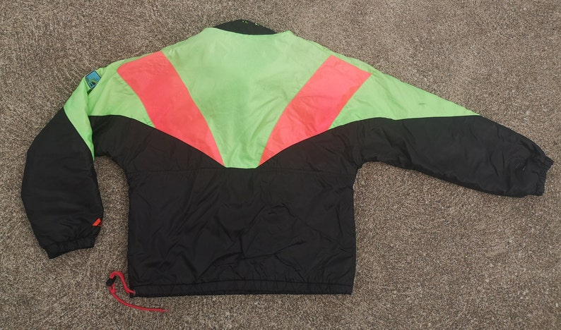 Pode incluir: Casaco corta-vento preto, verde e rosa com fecho de correr.