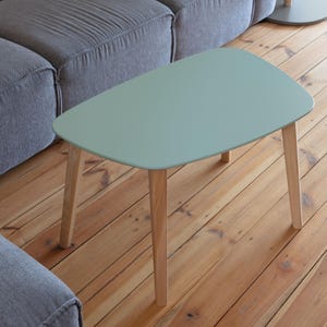 Może przedstawiać: Owalny stolik kawowy w jasnoniebieskim kolorze z drewnianymi nogami. Stolik stoi na drewnianej podłodze.