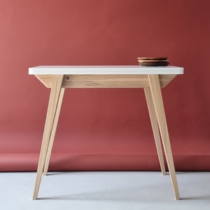 extendable console table made from solid wood legs and bottom in natural wooden color and white top. the top consist of two leaves which can be turned and oppened to double the top space