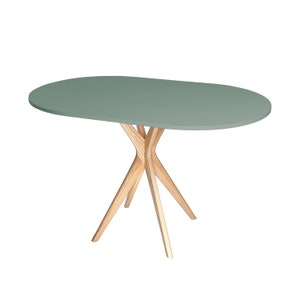 Op de afbeelding: Een lichtgroene ovale tafel met een houten onderstel. Het onderstel heeft vier poten die in een X-vorm met elkaar verbonden zijn.