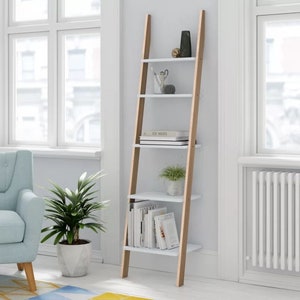 Op de afbeelding: Een witte ladderplank met bruine houten zijkanten. De plank heeft vier planken en is versierd met boeken, planten en decoratieve items.