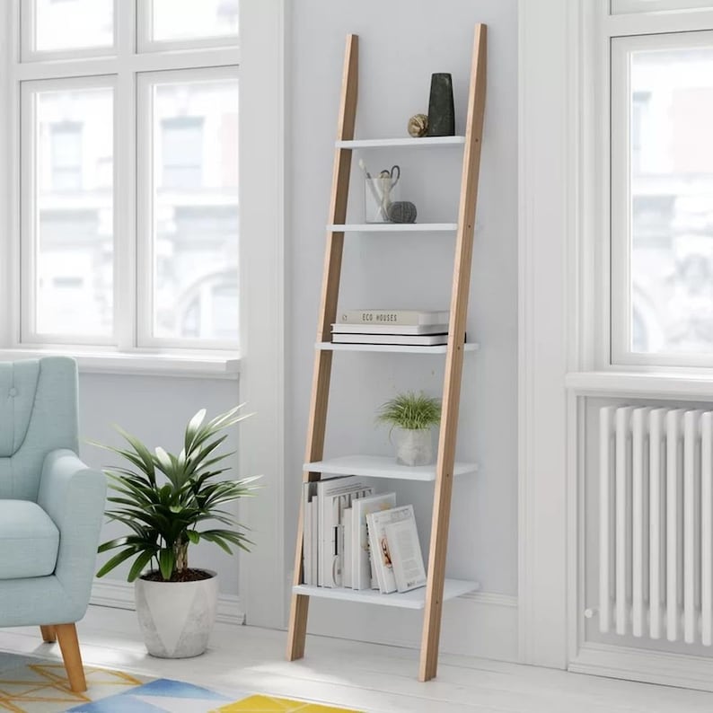Op de afbeelding: Een witte ladderplank met bruine houten zijkanten. De plank heeft vier planken en is versierd met boeken, planten en decoratieve items.
