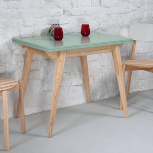 Może przedstawiać: Jasnozielony stół z drewnianą ramą i czterema nogami. Stół jest nakryty dwoma czerwonymi szklankami.