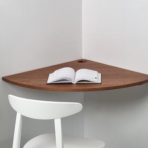 Könnte beinhalten: Ein Ecktisch mit einer Holzplatte und einem weißen Stuhl. Ein Buch liegt offen auf dem Tisch.