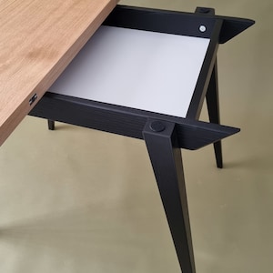 May include: A black wooden table with a light wood top and a pull-out drawer. The table has four legs that are angled outwards.