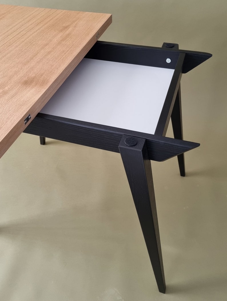 May include: A black wooden table with a light wood top and a pull-out drawer. The table has four legs that are angled outwards.