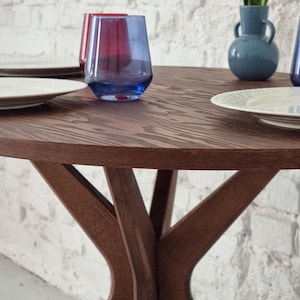 May include: A round wooden table with a dark brown finish and a unique X-shaped base. Two clear glasses with blue and red hues are on the table, along with two white plates.