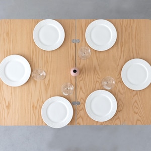 May include: A wooden folding table set with six white plates and four wine glasses. The table is ready for a dinner party.