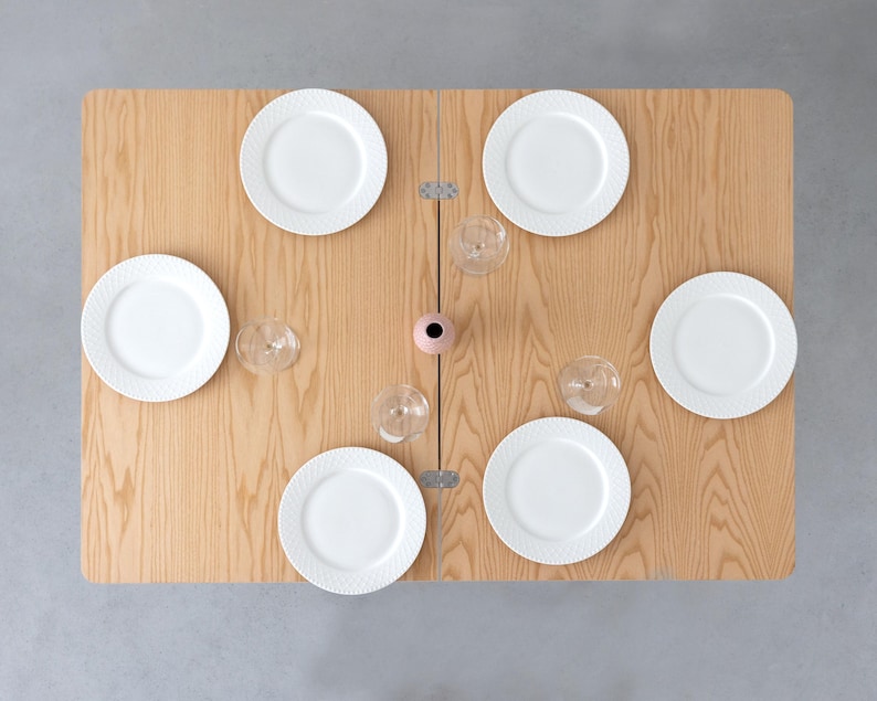 May include: A wooden folding table set with six white plates and four wine glasses. The table is ready for a dinner party.