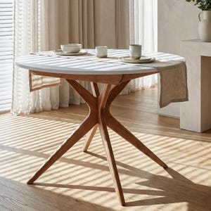 Może przedstawiać: Okrągły stół jadalniany z białym blatem i podstawą z naturalnego drewna. Stół ma unikalny wzór nóg w kształcie gwiazdy. Stół jest nakryty neutralną zastawą stołową i lnianym bieżnikiem. Stół ma średnicę około 122 cm.