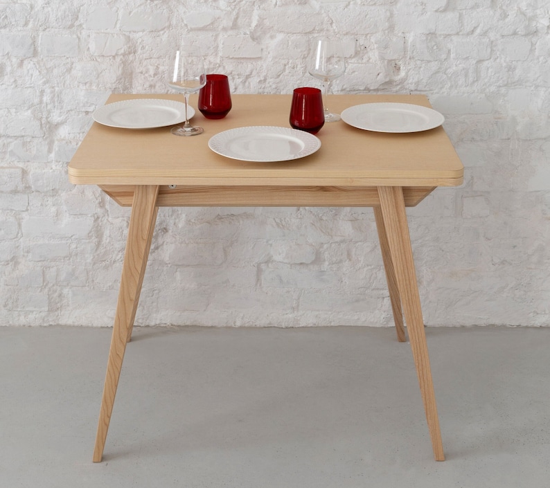 Small extendable dining table with wooden legs and ash veneered top. Kleiner Esstisch mit Holzbeinen und Eschenfurnierplatte mit einfachem Verlängerungssystem.Petite table à manger avec pieds en bois et plateau plaqué frêne.