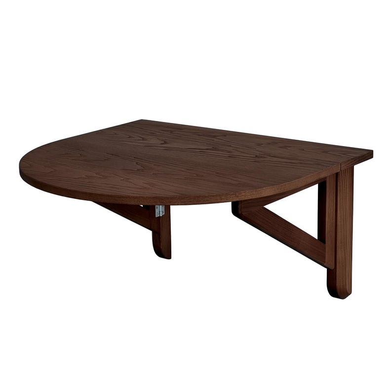 May include: A wall-mounted, semi-circular wooden table with a dark brown finish and visible wood grain. The table features a flat, straight back edge for mounting and two angled support brackets underneath that extend to the wall for stability.