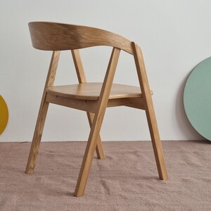 May include: A wooden chair with a curved back and a simple design. The chair is made of light brown wood and has a natural finish.