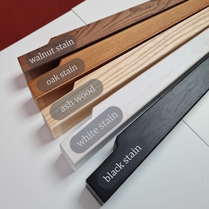 May include: Five wooden samples stained in different colors: walnut, oak, ash, white, and black. The samples are arranged in a row from darkest to lightest.