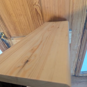 May include: A close-up of a light wood shelf with a rounded edge. The shelf is made of natural wood with a smooth finish.