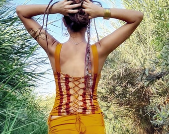 Peut inclure: Une femme portant une robe jaune moutarde avec un corsage à motifs marrons et blancs. Le corsage a un dos lacé. La robe est asymétrique et a une jupe fluide.