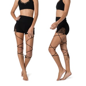 Puede incluir: Sujetador deportivo negro con diseño cruzado y shorts negros a juego con detalle de encaje. Los shorts tienen cintura alta y están atados a las piernas con correas negras.