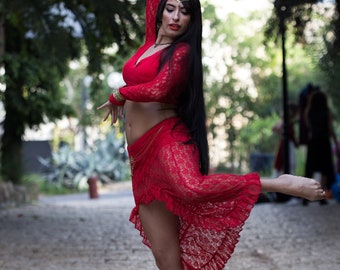 May include: A woman in a red lace dress with a gold headpiece and jewelry dances in a park setting.