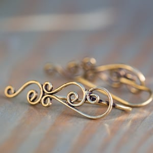 May include: A pair of gold-toned ear cuffs with a delicate, swirling design. The cuffs are made of thin wire and have a simple, elegant look.