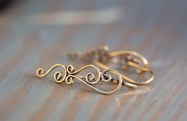 May include: A pair of gold-toned ear cuffs with a delicate, swirling design. The cuffs are made of thin wire and have a simple, elegant look.