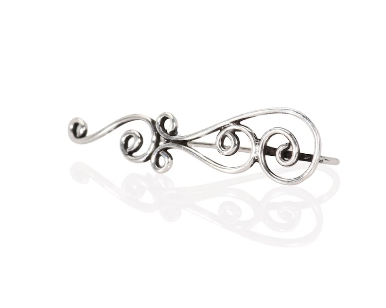 May include: Silver ear cuff with a delicate, swirling design. The cuff is made of a single piece of metal and has a simple, elegant look.