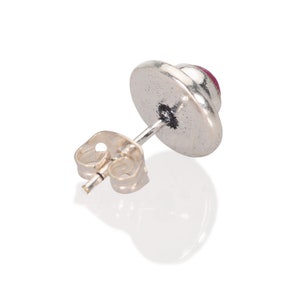 May include: Silver stud earring with a round, red gemstone.
