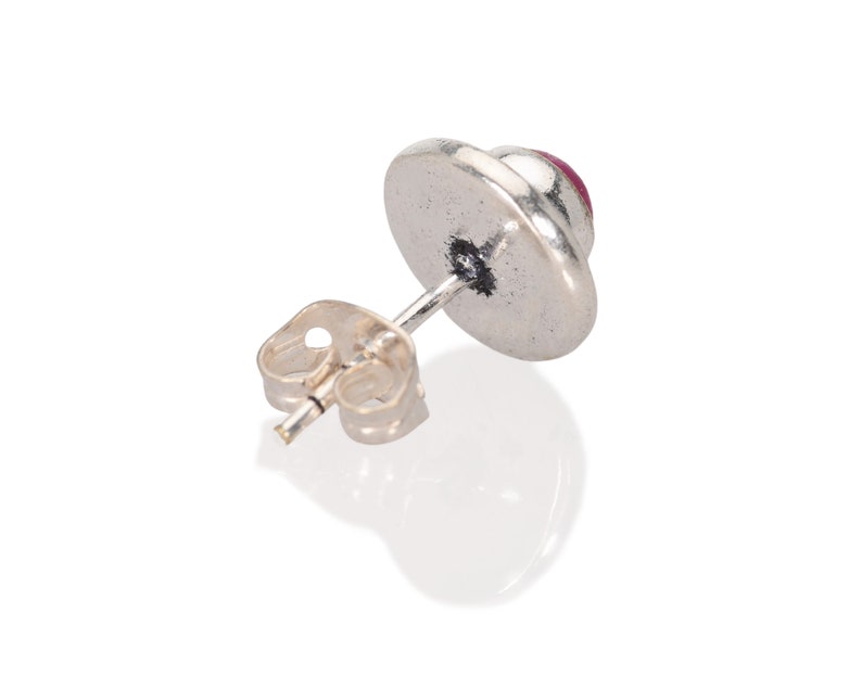 May include: Silver stud earring with a round, red gemstone.