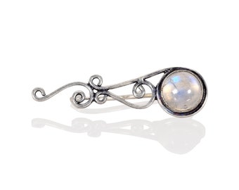May include: A silver brooch with a delicate, swirling design and a round, iridescent moonstone.