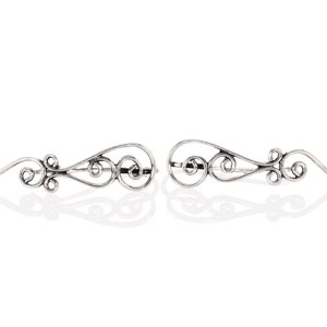 May include: A pair of silver ear cuffs with a delicate, swirling design. The cuffs are made of thin metal and have a slightly curved shape.