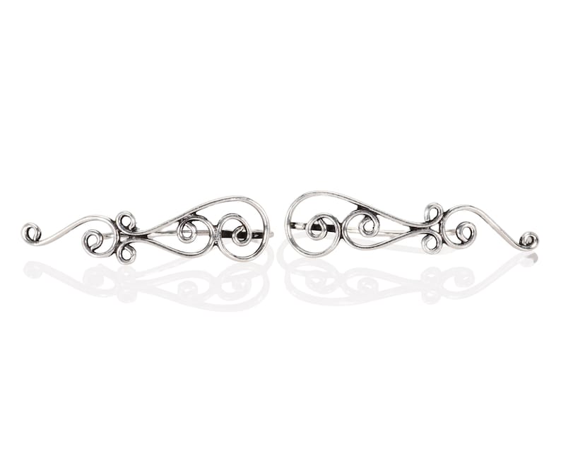 May include: A pair of silver ear cuffs with a delicate, swirling design. The cuffs are made of thin metal and have a slightly curved shape.
