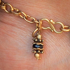 May include: A gold chain bracelet with a black bead charm. The charm is made of small gold beads and a black stone.