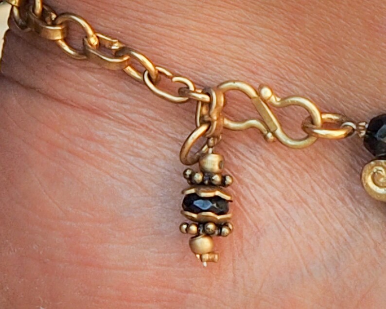May include: A gold chain bracelet with a black bead charm. The charm is made of small gold beads and a black stone.