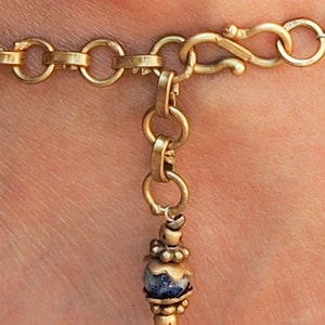 May include: Gold chain anklet with a blue and white stone charm and a lobster clasp closure.