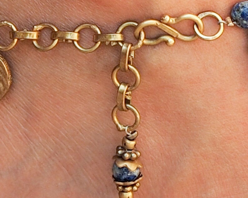 May include: Gold chain anklet with a blue and white stone charm and a lobster clasp closure.