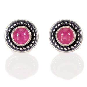 Puede incluir: Un par de pendientes de plata con una piedra preciosa rosa engastada en un engaste de plata. Los pendientes tienen un borde decorativo.