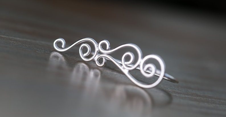 May include: A silver filigree ring with a delicate, swirling design. The ring is made of thin wire and has a simple, elegant look.