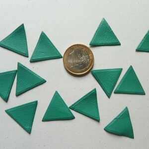 May include: Ten teal green felt triangles arranged in a circle around a single euro coin. The triangles are all the same size and shape.