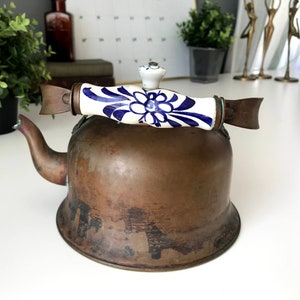 May include: A vintage copper kettle with a blue and white porcelain handle and lid. The kettle has a worn, aged patina.