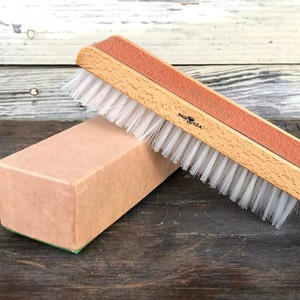 May include: A wooden brush with white bristles and a red and brown handle. The brush is labeled "Made in U.S.A." and is resting on a brown cardboard box.
