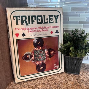 May include: A vintage Tripoley board game box featuring the text Tripoley The original game of Michigan Rummy Hearts and Poker Deluxe Layout Only. The box cover displays an illustration of four people playing the game around a circular board.
