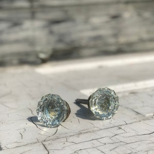 May include: Two clear glass door knobs with a textured surface and a silver metal stem.