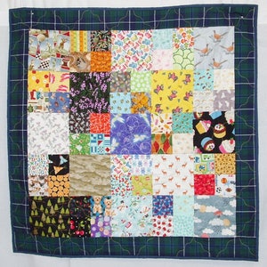 May include: A colorful patchwork quilt with a variety of patterns and designs. The quilt is made up of many small squares, each with a different fabric. The quilt is bordered with a dark blue fabric with a plaid pattern.