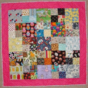 May include: A pink patchwork quilt with a variety of colorful squares featuring different patterns and designs, including animals, letters, numbers, and toys.