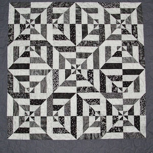 May include: Black and white quilt with a geometric pattern. The quilt is made up of squares and triangles, and the pattern creates a sense of movement and depth.