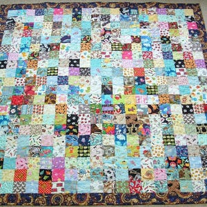 May include: A patchwork quilt with a variety of colorful fabric squares. The quilt features a dark blue border with a paisley design. The squares are in various colors and patterns, including floral, animal, and geometric designs. A handmade, cozy blanket.