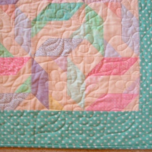 May include: A pastel pink, green, and purple patchwork quilt with a teal polka dot border.
